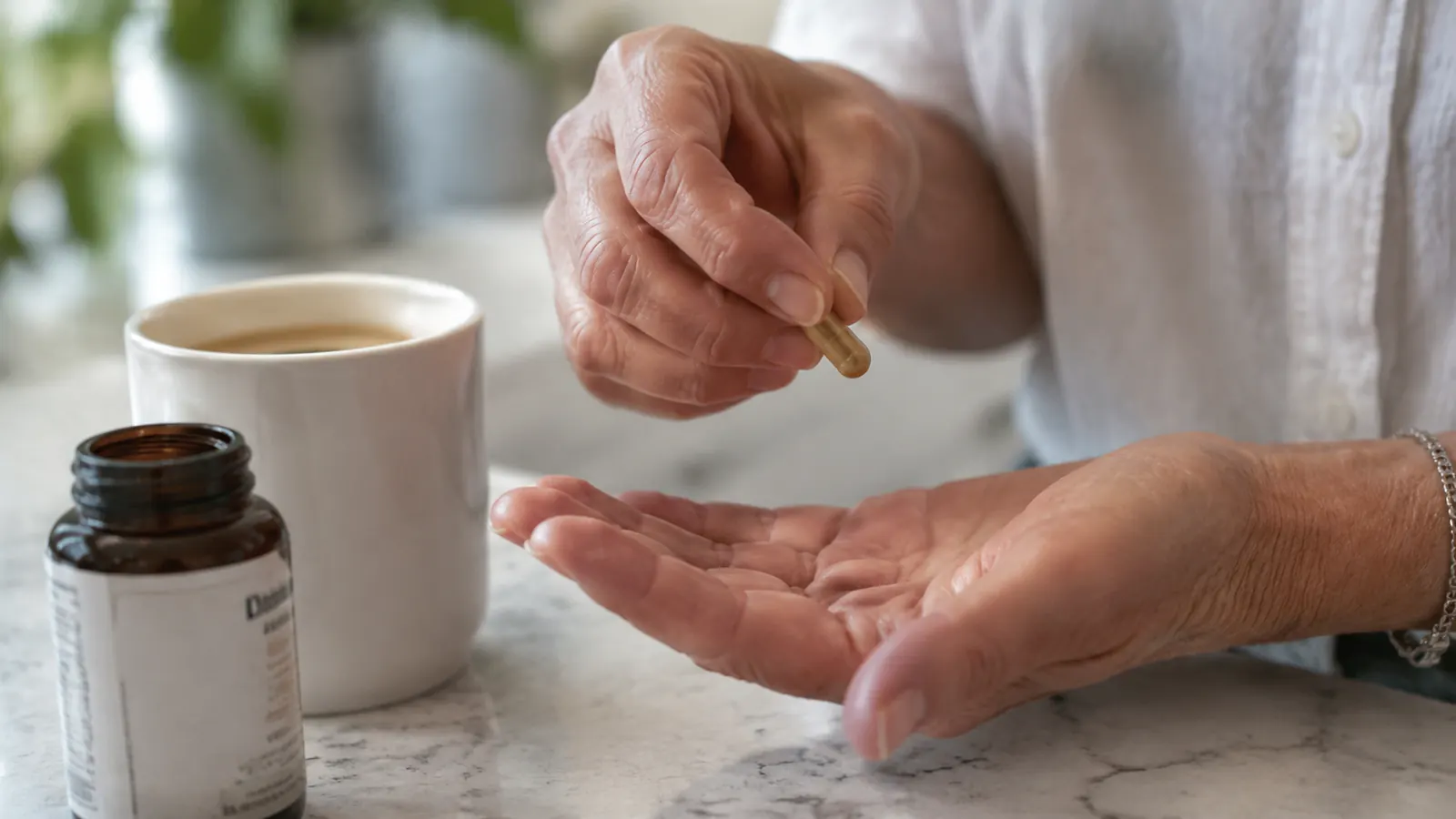 A hand holding a capsule above an open palm next to a mug of coffee on a kitchen counter